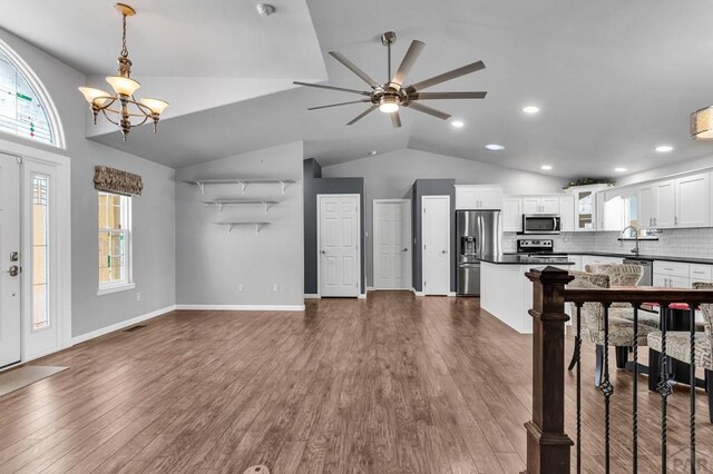 interior space with visible vents, baseboards, dark wood finished floors, vaulted ceiling, and ceiling fan with notable chandelier