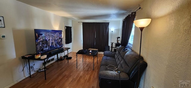 living area featuring a textured wall, baseboards, and wood finished floors