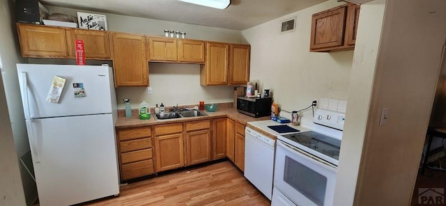 kitchen with light countertops, visible vents, light wood-style flooring, a sink, and white appliances