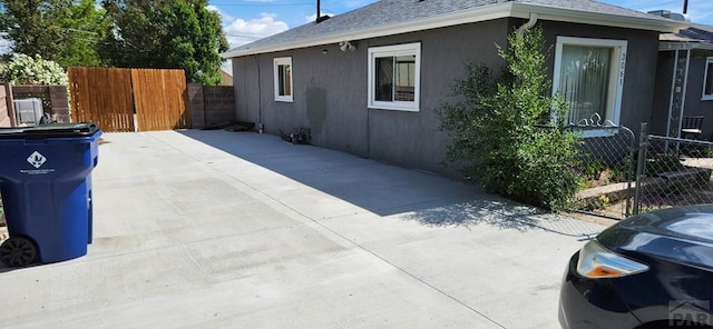 view of side of property featuring a patio, roof with shingles, fence, and stucco siding