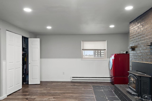 interior space featuring laundry area, a wainscoted wall, a baseboard radiator, wood finished floors, and a wood stove