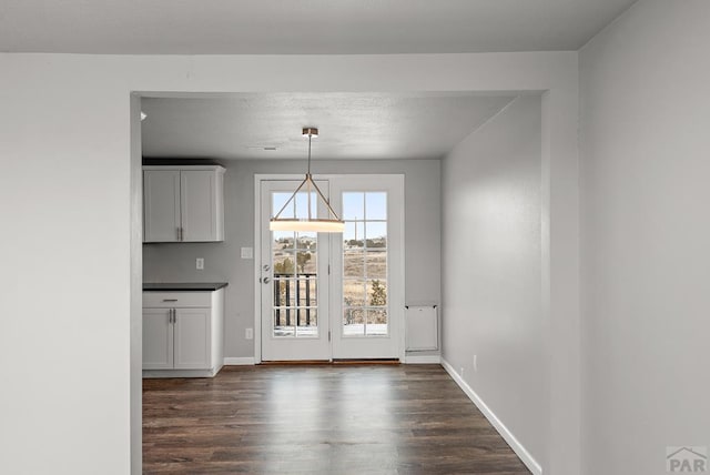 unfurnished dining area with baseboards and dark wood finished floors