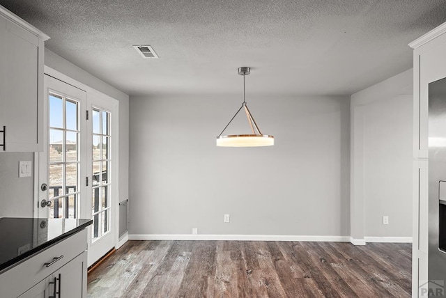 unfurnished dining area featuring dark wood-type flooring, visible vents, a textured ceiling, and baseboards