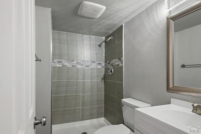 full bathroom featuring vanity, tiled shower, and a textured wall