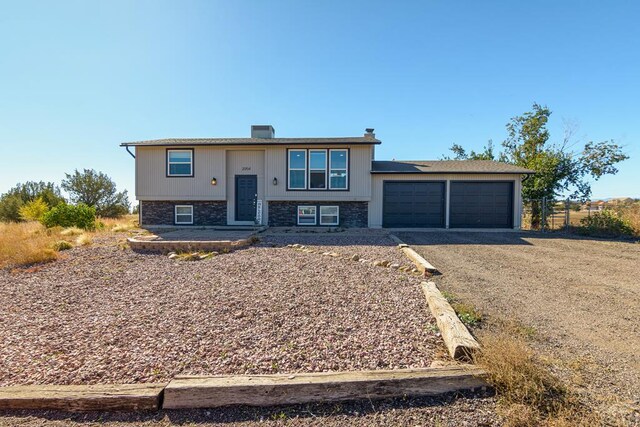 raised ranch featuring a garage, gravel driveway, and solar panels