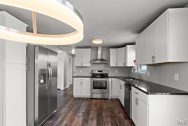 kitchen featuring white cabinets, dark countertops, stainless steel appliances, wall chimney range hood, and a sink