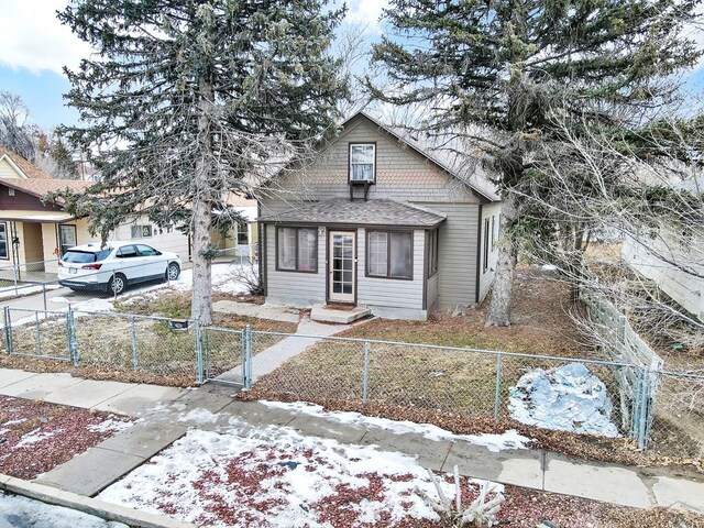 bungalow-style home with a fenced front yard, a garage, driveway, roof with shingles, and a gate