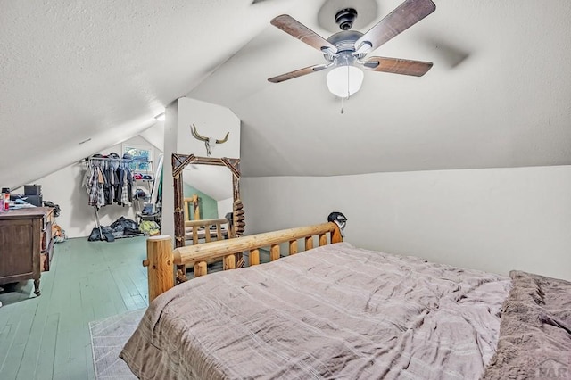 bedroom featuring a ceiling fan, vaulted ceiling, a textured ceiling, and wood finished floors