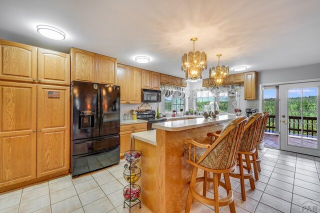 kitchen featuring light tile patterned flooring, a kitchen island, light countertops, black appliances, and decorative light fixtures