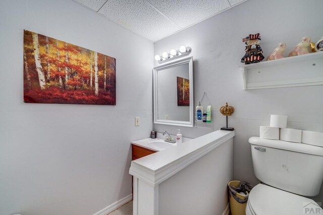 bathroom with a drop ceiling, vanity, toilet, and baseboards