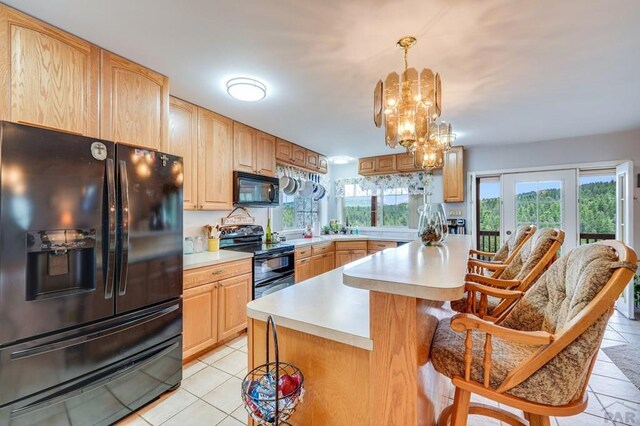 kitchen featuring a kitchen island, a breakfast bar area, light countertops, black appliances, and pendant lighting