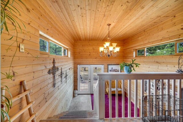 staircase with a chandelier, french doors, wooden ceiling, and wooden walls