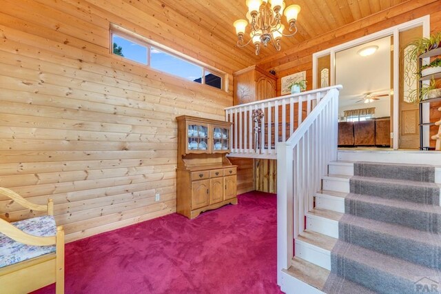 staircase with an inviting chandelier, carpet, wood ceiling, and wooden walls