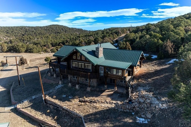 rear view of property featuring stone siding, metal roof, a chimney, log siding, and a wooded view