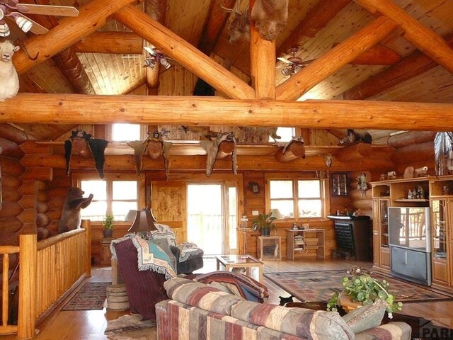 living room featuring log walls, a ceiling fan, wood finished floors, wooden ceiling, and beamed ceiling