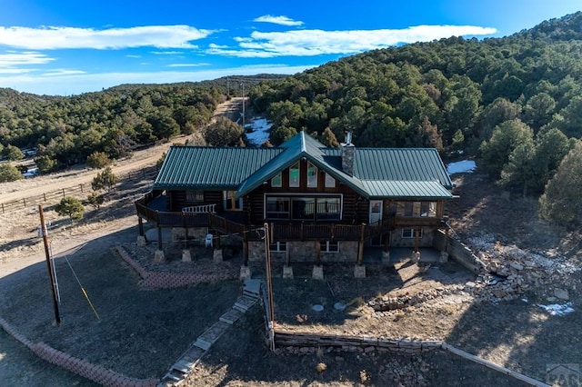 back of property featuring a chimney, a standing seam roof, metal roof, a view of trees, and stone siding