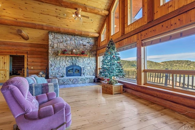 living area with light wood-style floors, wood ceiling, a mountain view, a stone fireplace, and high vaulted ceiling