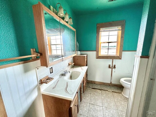 bathroom featuring toilet, wainscoting, plenty of natural light, and vanity