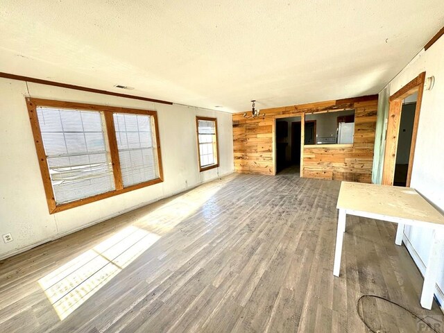 unfurnished living room with a textured ceiling, wooden walls, visible vents, and wood finished floors