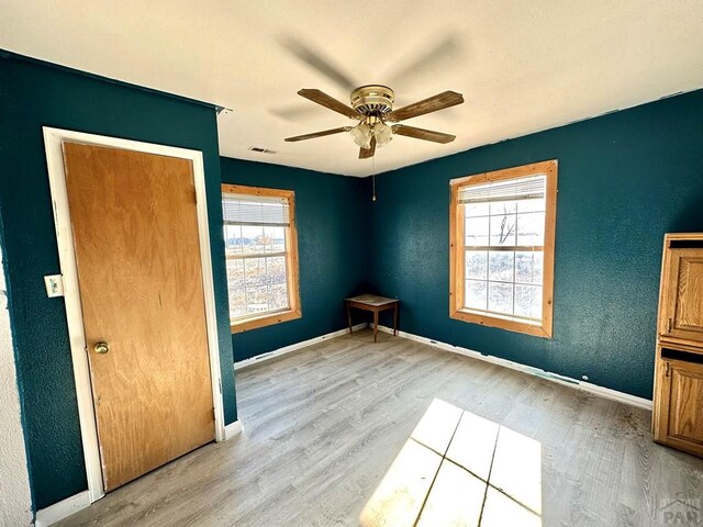 spare room with light wood-type flooring, a healthy amount of sunlight, visible vents, and baseboards