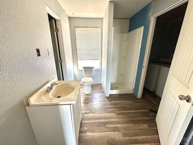 full bathroom featuring a textured wall, wood finished floors, a shower stall, and vanity