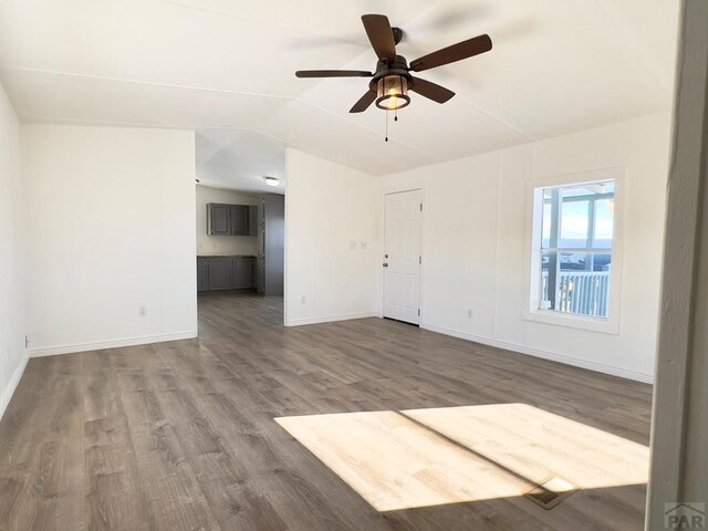 empty room with lofted ceiling, ceiling fan, wood finished floors, and baseboards