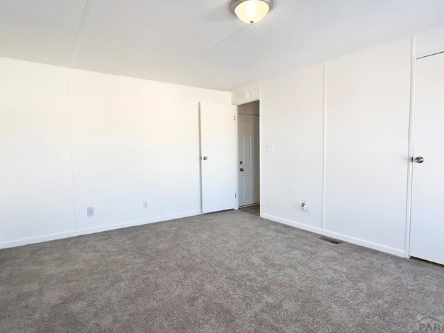 spare room featuring visible vents and dark colored carpet