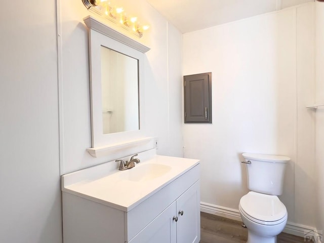 half bathroom featuring baseboards, vanity, toilet, and wood finished floors