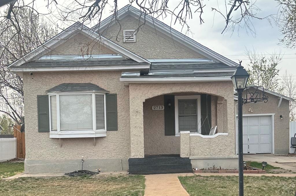 view of front facade with a porch, fence, an attached garage, and stucco siding