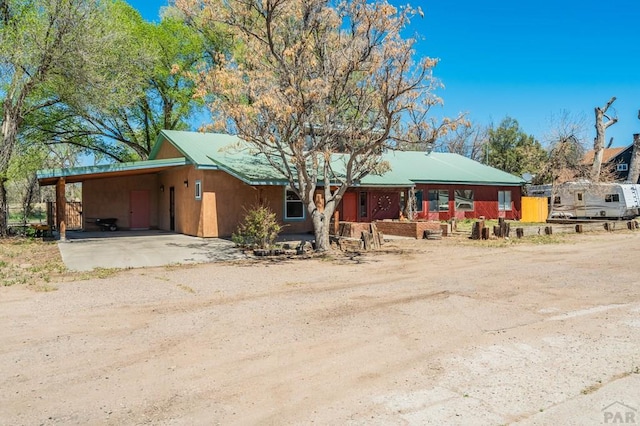 ranch-style home with dirt driveway and an attached carport
