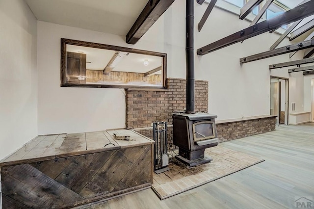 interior space with a wood stove, wood finished floors, and beamed ceiling