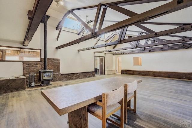 dining area with high vaulted ceiling, wood finished floors, a wood stove, and beamed ceiling