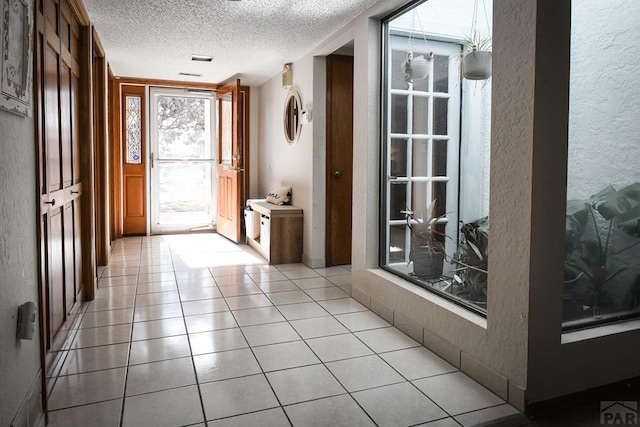 doorway featuring a textured ceiling, a textured wall, and light tile patterned floors