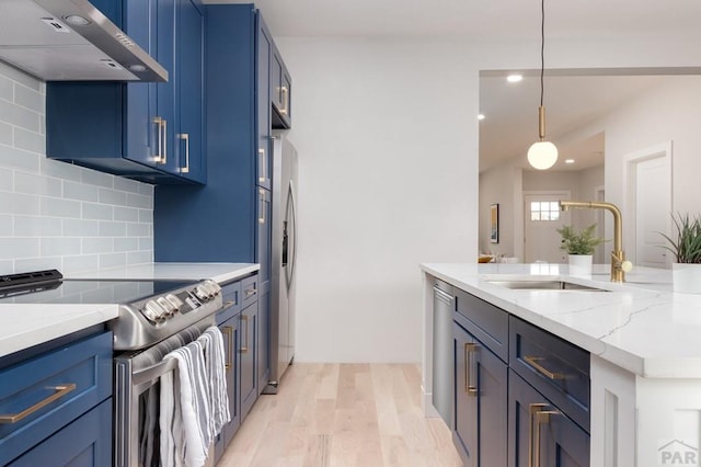 kitchen with light stone counters, decorative light fixtures, stainless steel appliances, a sink, and wall chimney exhaust hood