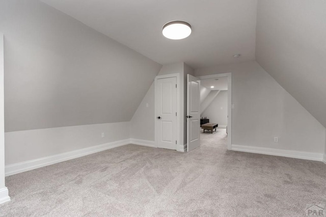 additional living space with light carpet, vaulted ceiling, and baseboards