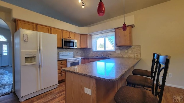 kitchen featuring white appliances, arched walkways, backsplash, a peninsula, and a sink