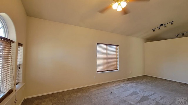 carpeted empty room featuring vaulted ceiling, rail lighting, ceiling fan, and baseboards