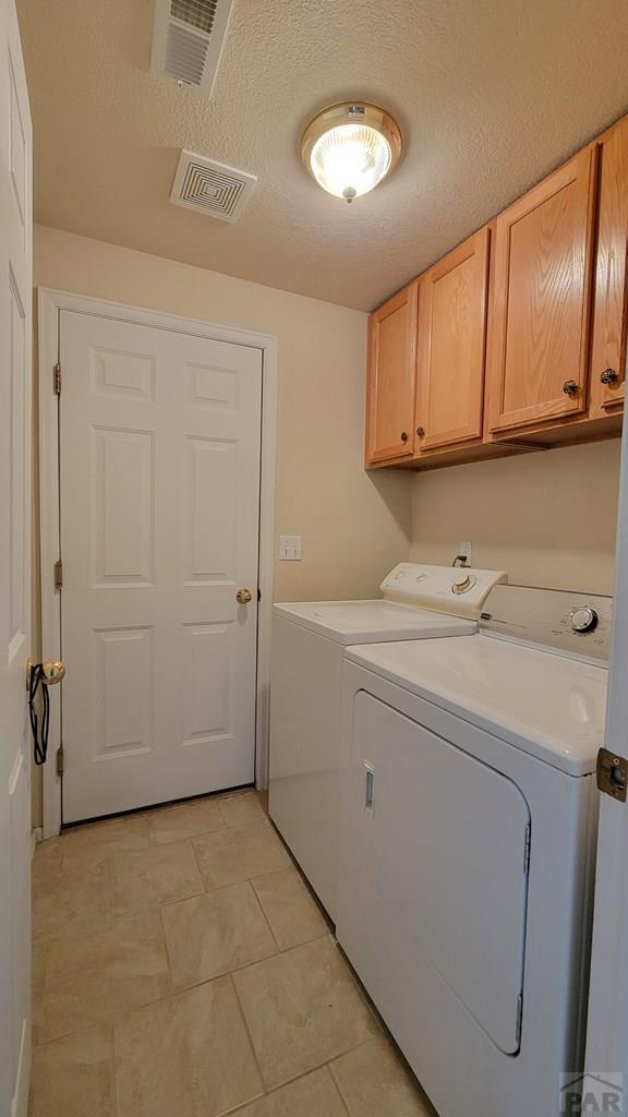 clothes washing area featuring visible vents, cabinet space, a textured ceiling, and washing machine and clothes dryer