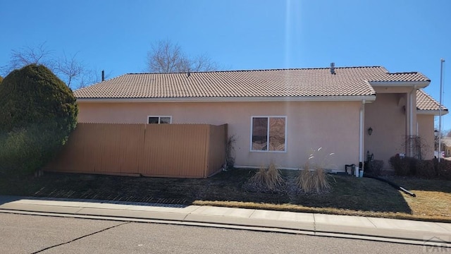 view of side of property featuring a tile roof, fence, and stucco siding