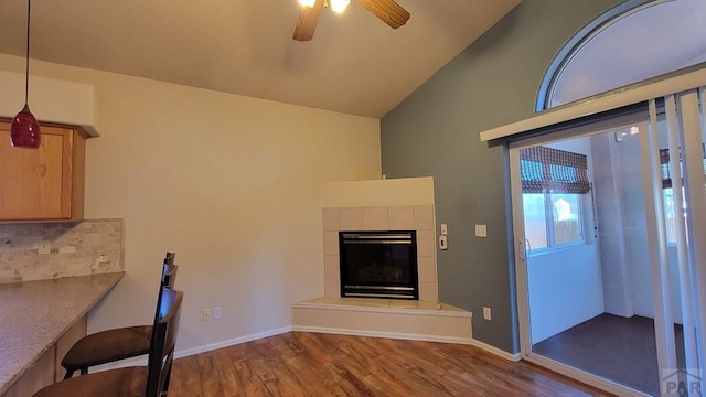 interior space with ceiling fan, wood finished floors, vaulted ceiling, a fireplace, and backsplash