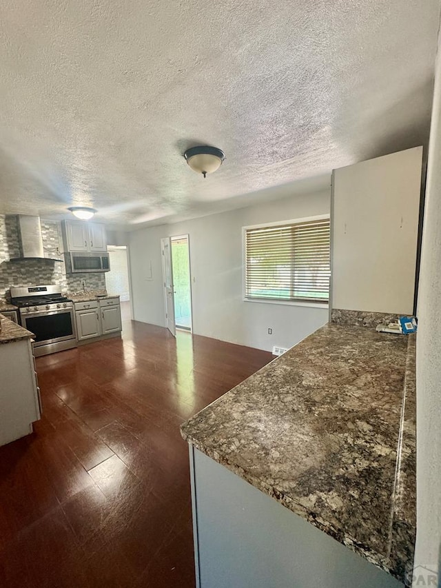 19 Cornell Cir, Pueblo, CO 81005 - kitchen featuring stainless steel appliances, wall chimney exhaust hood, a textured ceiling, backsplash, and a peninsula
