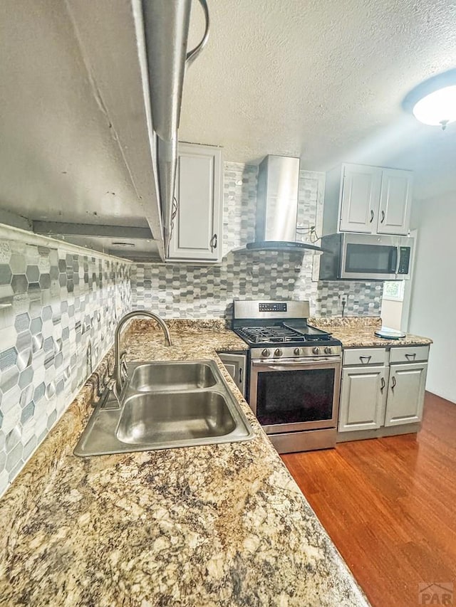 19 Cornell Cir, Pueblo, CO 81005 - kitchen with stainless steel appliances, wall chimney range hood, backsplash, wood finished floors, and a textured ceiling