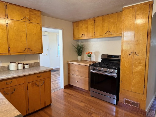 402 Alma Ave, Pueblo, CO 81004 - kitchen with stainless steel range with gas cooktop, wood finished floors, light countertops, brown cabinets, and a textured ceiling