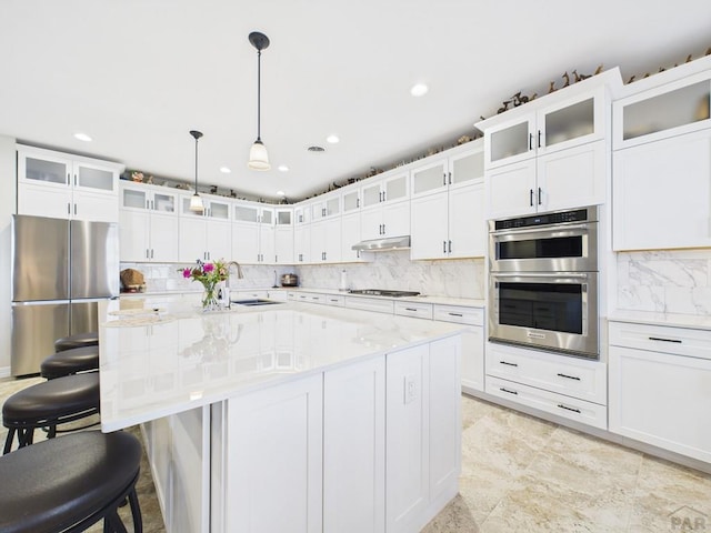 kitchen featuring a sink, backsplash, appliances with stainless steel finishes, under cabinet range hood, and white cabinets