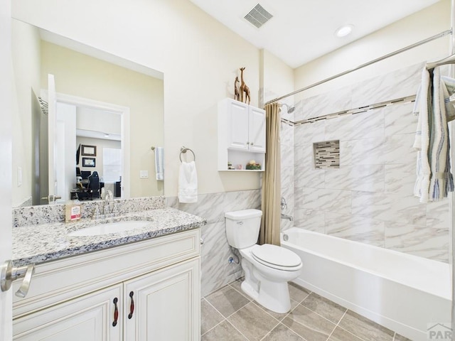 bathroom featuring tile walls, shower / bath combo, visible vents, toilet, and vanity