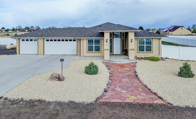 view of front of house featuring concrete driveway, stucco siding, fence, a garage, and a shingled roof