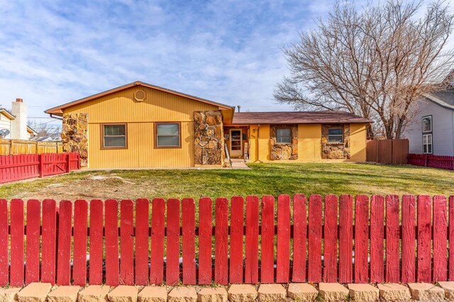 ranch-style house featuring stone siding, a front yard, and a fenced backyard