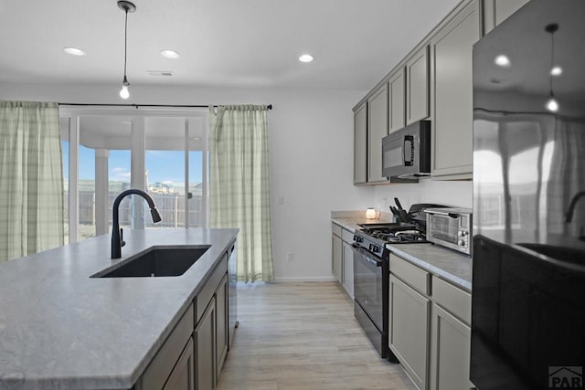 kitchen with a kitchen island with sink, a city view, a sink, black appliances, and pendant lighting