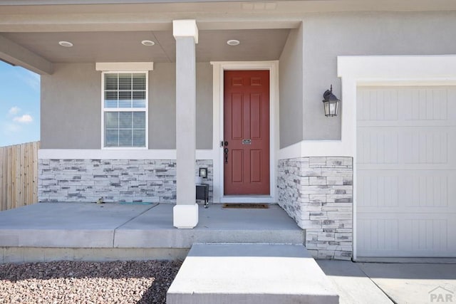 view of exterior entry with stone siding, a porch, and stucco siding