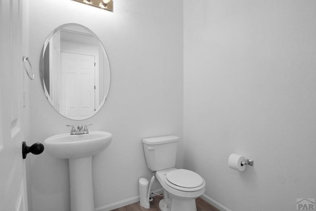 half bathroom with a sink, wood finished floors, toilet, and baseboards